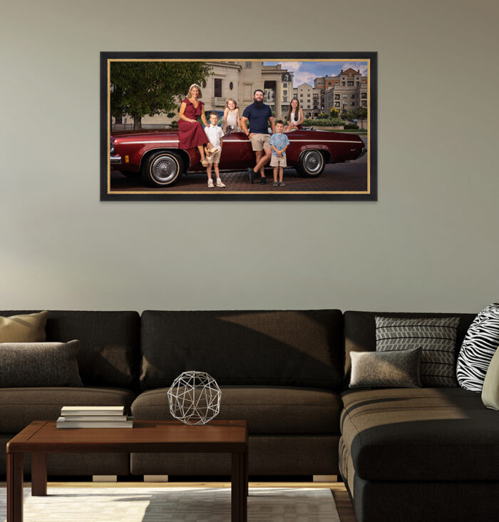 Framed family portrait with a maroon vintage convertible hanging above a sectional sofa in a living room