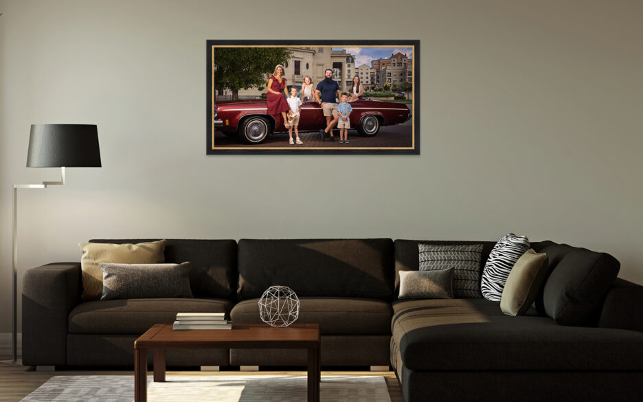 Framed family portrait with a maroon vintage convertible hanging above a sectional sofa in a living room