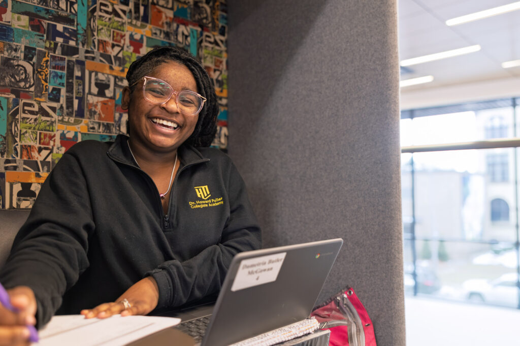 Howard Fuller Collegiate photography of a student smiling while working at a desk inside the school