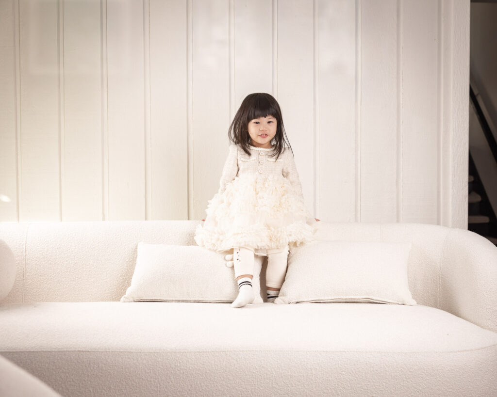 Two-year-old girl sitting on a sofa in natural light during an in-home family photography session