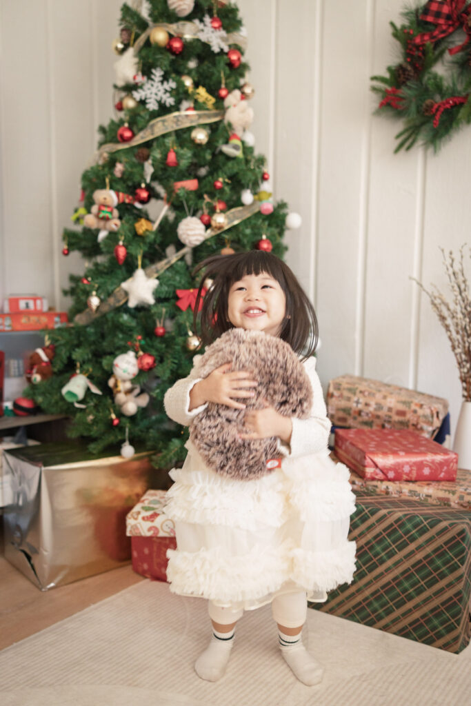 Toddler standing in front of a Christmas tree during an in-home family photography session