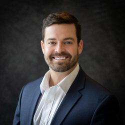 Professional headshot of a bearded man in a navy blazer on a dark backdrop