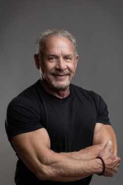 Personal branding headshot in a Carmel, Indiana studio: a smiling man in a black t-shirt with arms crossed on a gray backdrop