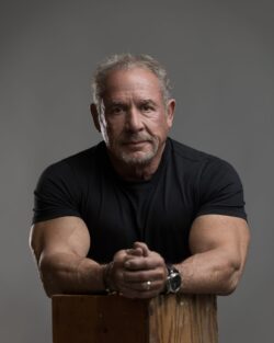 Personal branding portrait of a man leaning forward on a wooden box with hands clasped, gray studio backdrop near Indianapolis